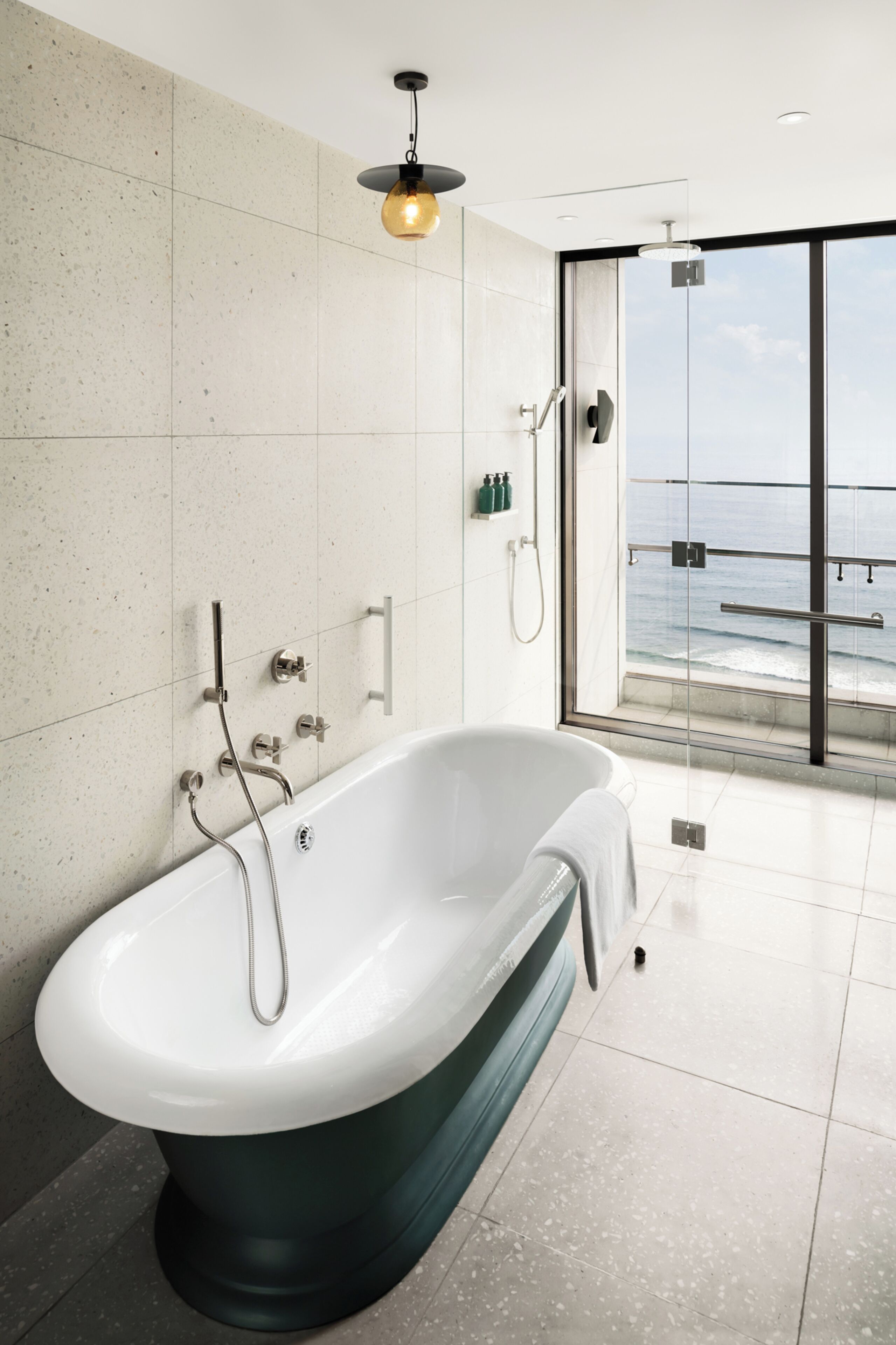 A modern bathroom with a freestanding bathtub, a glass shower enclosure, and a view of the ocean through a large window.