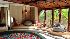 A room with a large pool filled with colorful plastic balls, a seating area with cushions, and a view of lush greenery through large windows. - New World Hoiana Beach Resort (Da Nang)