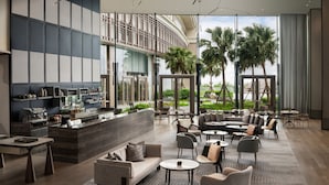 A modern hotel lobby with a bar area, seating arrangements, and large windows offering views of palm trees. - New World Hoiana Beach Resort (Da Nang)