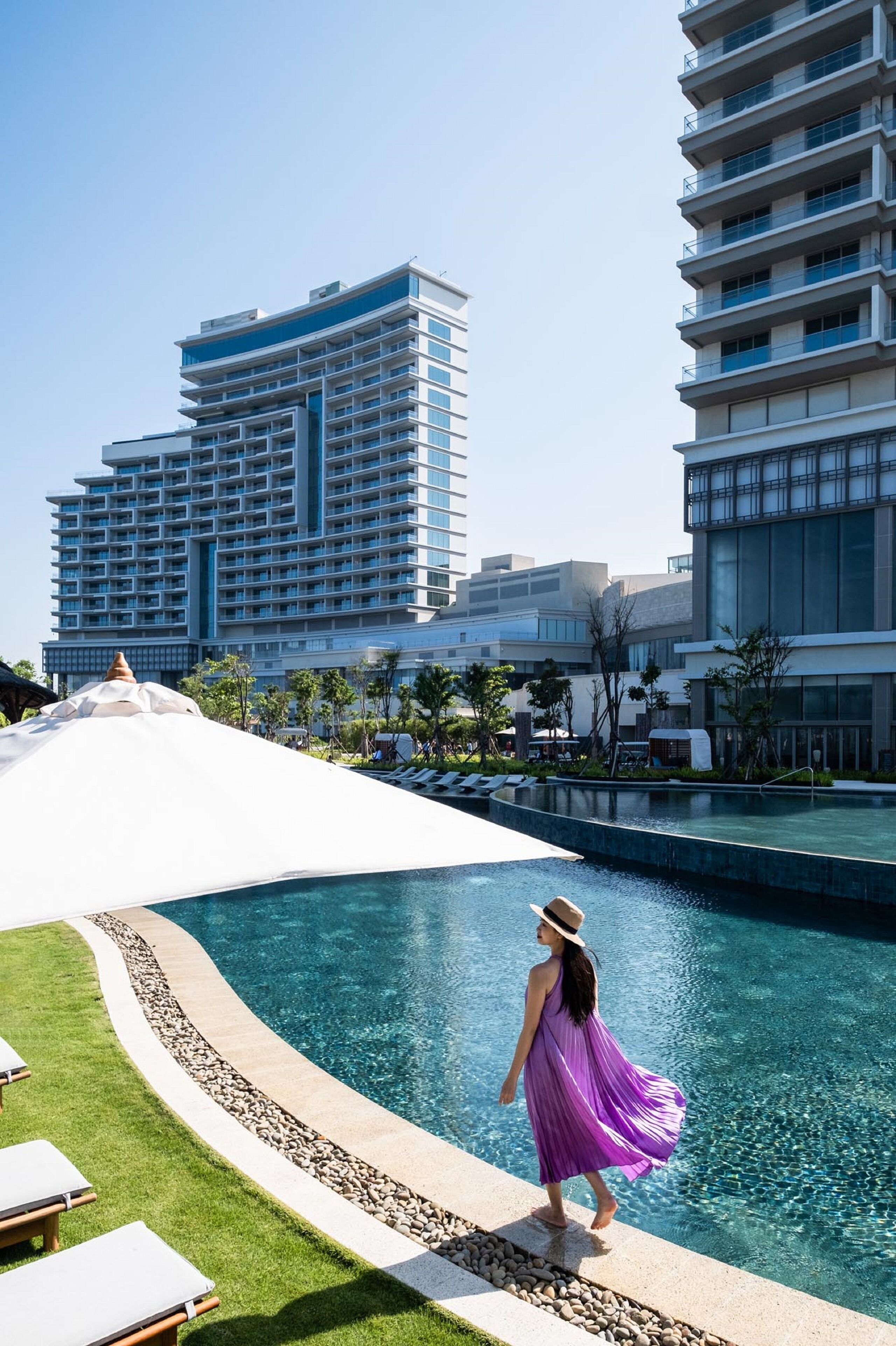 A pool area with lounge chairs and a person in a purple dress.