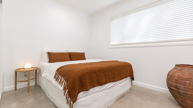 A bedroom with a bed, a bedside lamp, a window with blinds, and a large vase. - Stunning, Sleek and Refined, The Black Beach House is perfection from the time you walk through the (Elizabeth Beach)