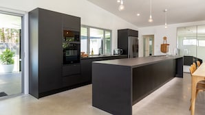 A modern kitchen with dark cabinetry, a central island, and a dining area with wooden chairs. - Stunning, Sleek and Refined, The Black Beach House is perfection from the time you walk through the (Elizabeth Beach)