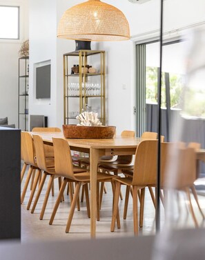 Een moderne eetruimte met een ronde houten tafel, zes houten stoelen en een grote geweven hanglamp.