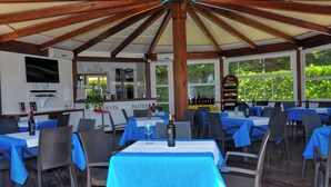 An outdoor dining area with tables covered in blue tablecloths, wicker chairs, and a wooden ceiling structure. - Tenuta Paifer (Otranto)