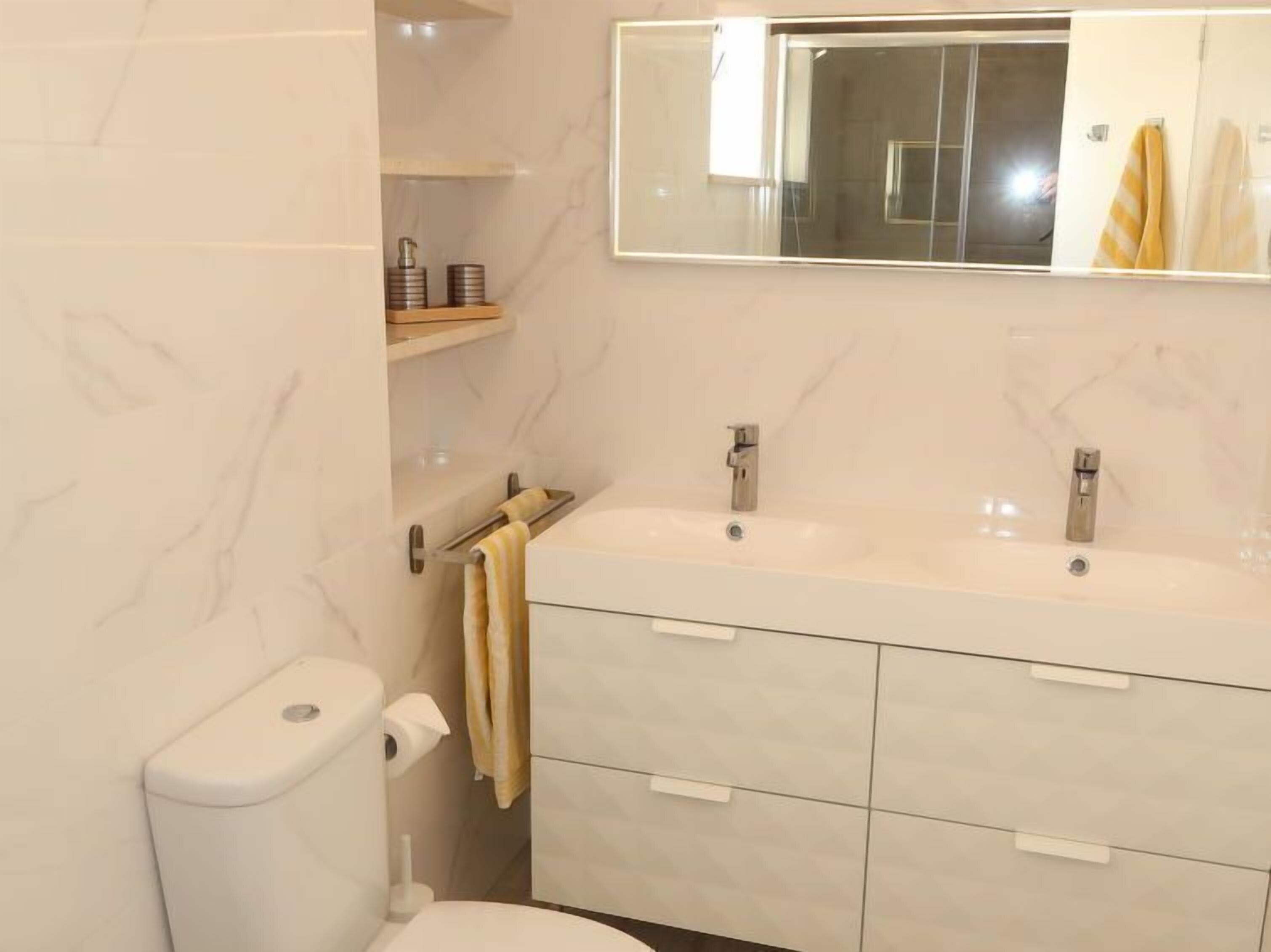 A modern bathroom with two sinks, a toilet, and a mirror.