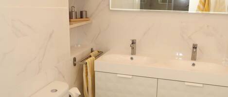 A modern bathroom with two sinks, a toilet, and a mirror.