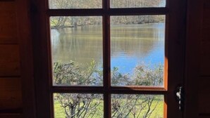 Une vue à travers une fenêtre à cadre en bois, qui révèle un lac paisible et des arbres en arrière-plan.
