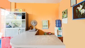 A kitchen with a white countertop, a fan, a water dispenser, and a calendar on the wall. - Hotel O Wisma Heksa (Batam)