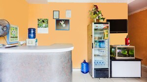 A reception area with a counter, a fan, a water dispenser, a refrigerator, a fish tank, and a fire extinguisher. - Hotel O Wisma Heksa (Batam)
