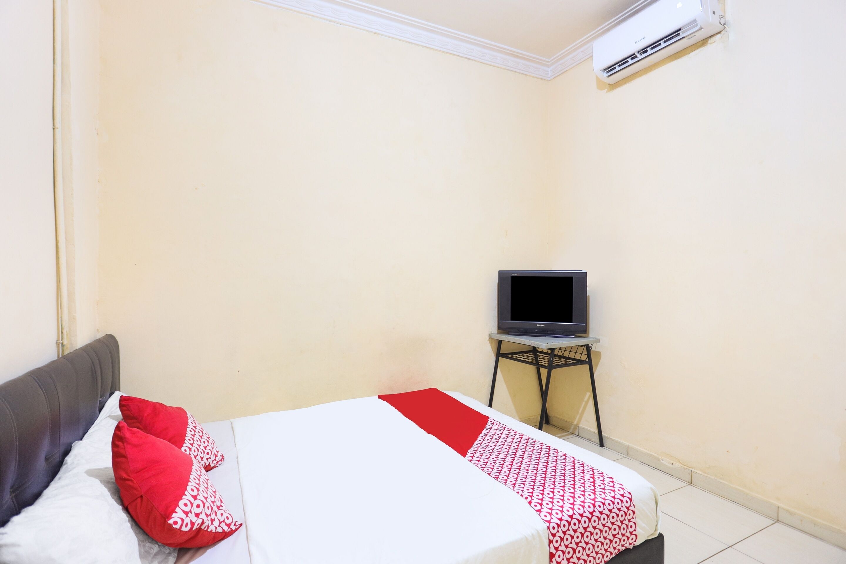 A bedroom with a bed, a television on a stand, and an air conditioning unit on the wall.