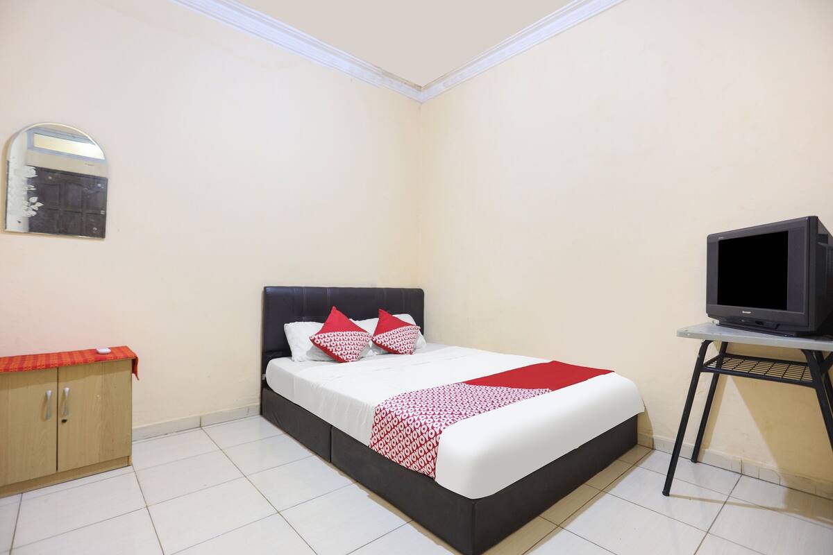 A neatly arranged bedroom with a bed, a television on a stand, and a small cabinet.