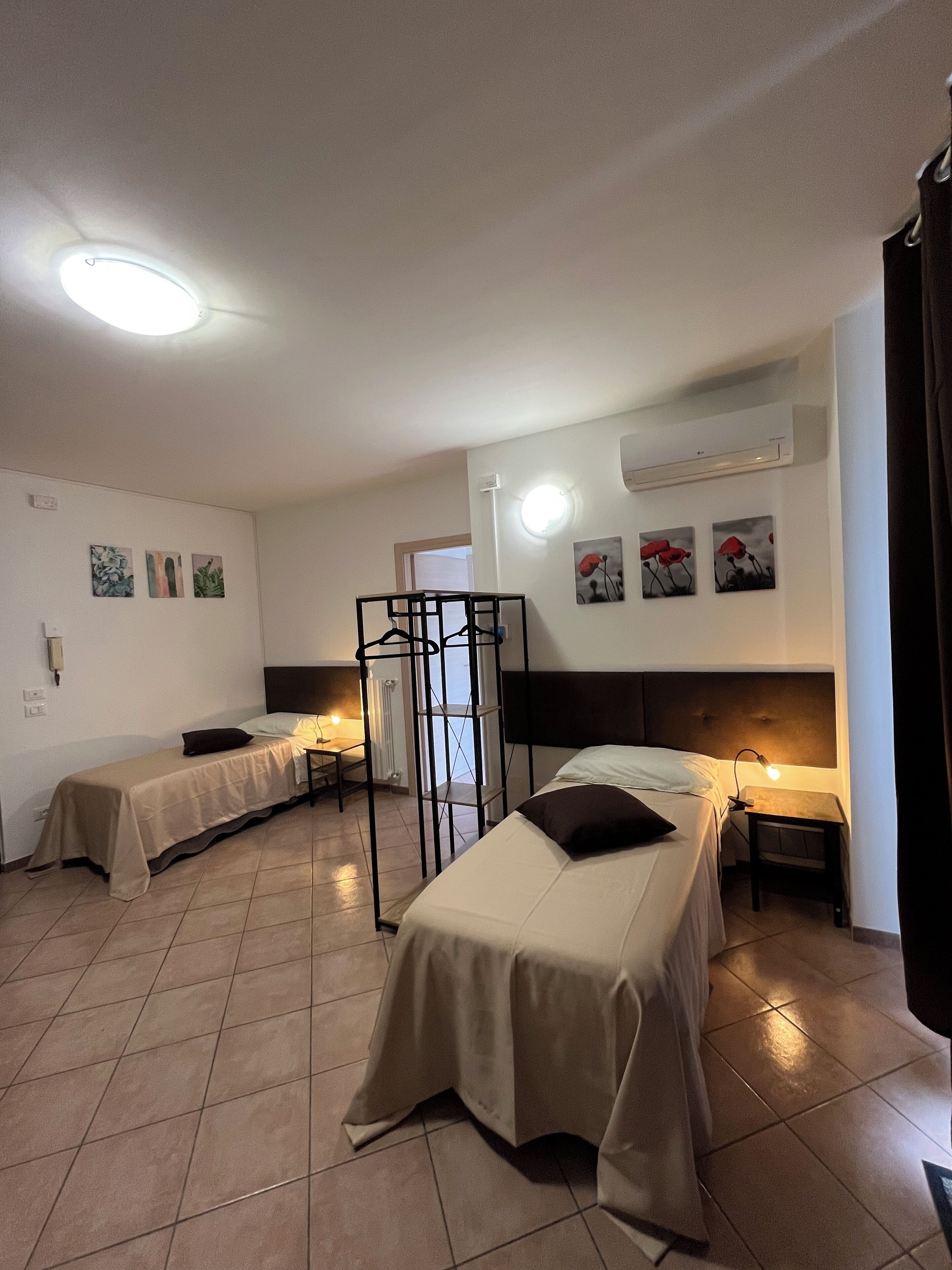 A room with two beds, a small table, and a chair. There are wall-mounted air conditioning units and a ceiling light.