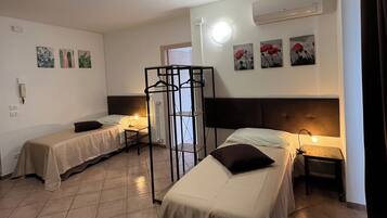 A room with two beds, a small table, and a chair. There are wall-mounted air conditioning units and a ceiling light.