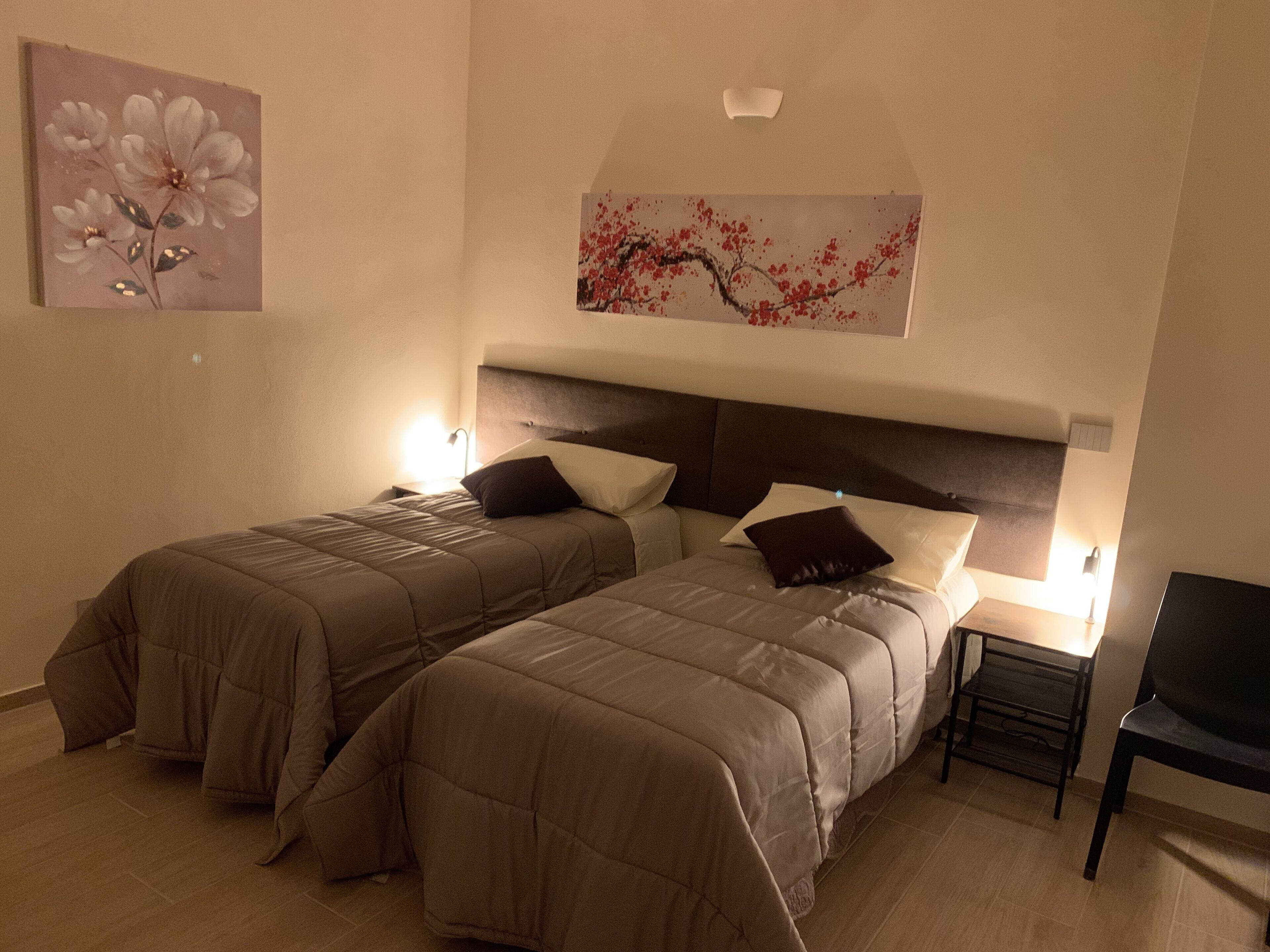 A hotel room with two beds, a nightstand, a chair, and artwork on the walls.