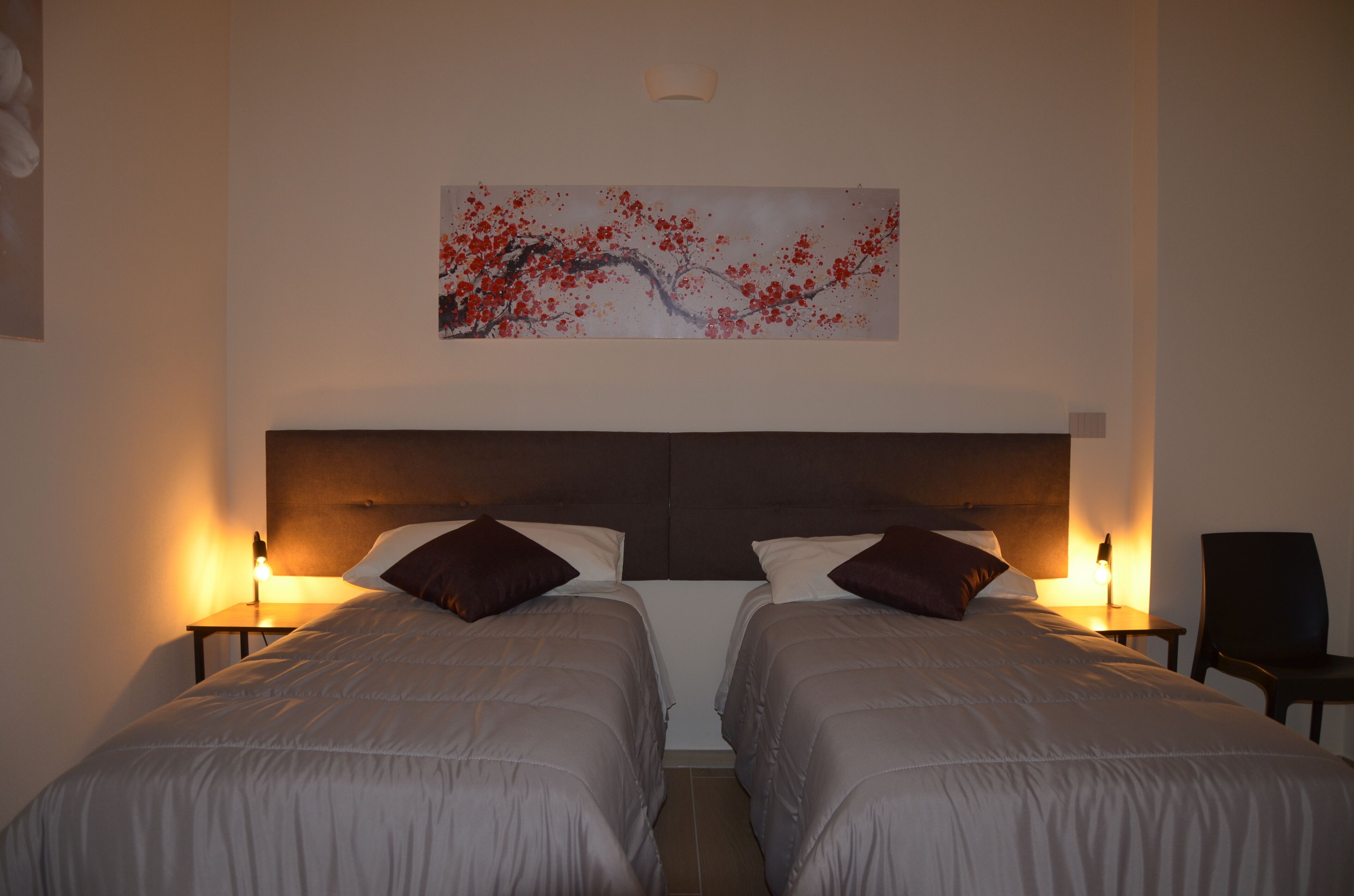 A hotel room with two beds, a large painting on the wall, and bedside lamps.