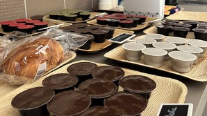 Uma bancada de cozinha com diversos alimentos e recipientes, incluindo uma barra de pão, chocolates e uma máquina de café.