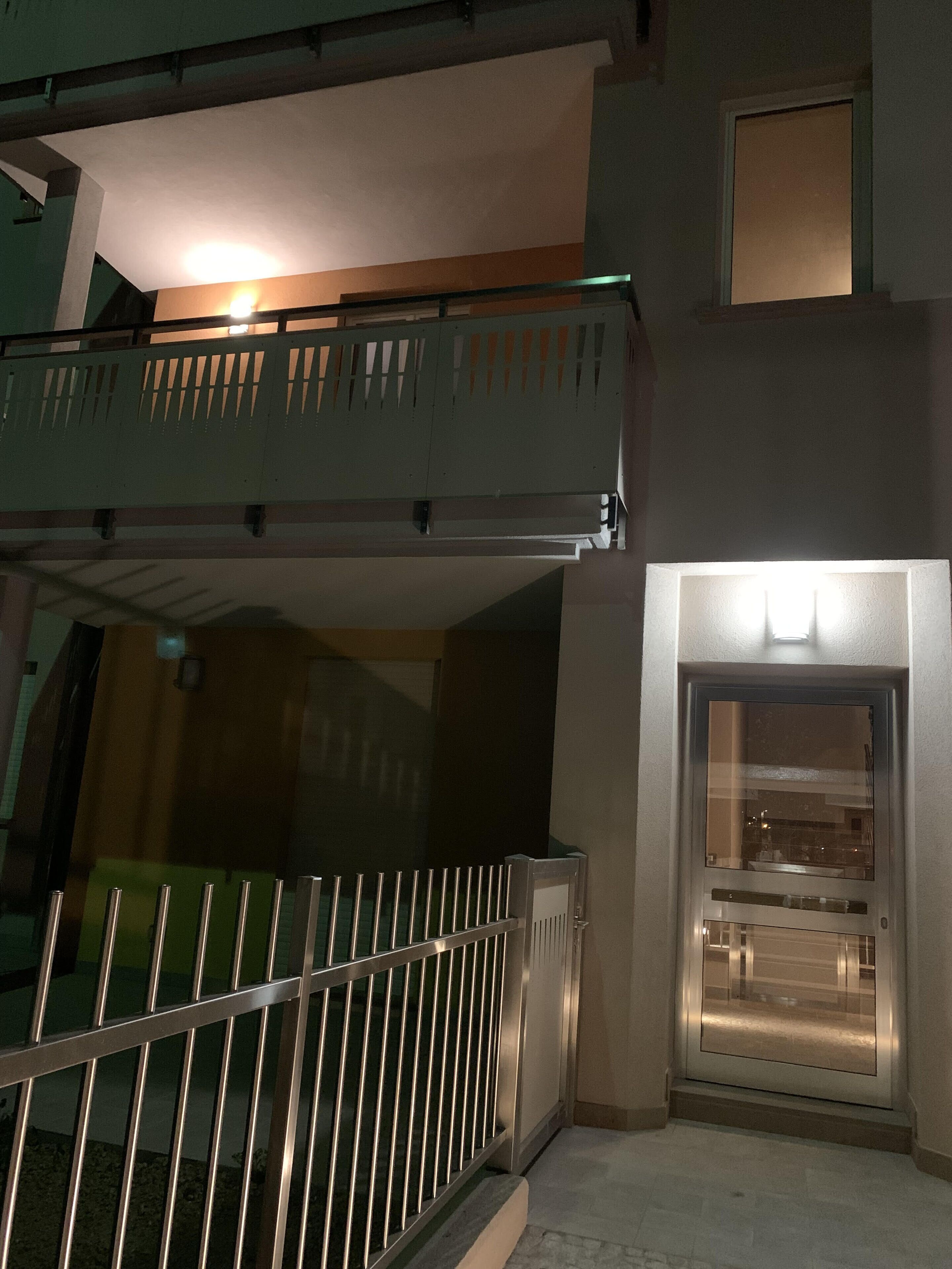 A modern building with a balcony, a glass door, and a metal railing.