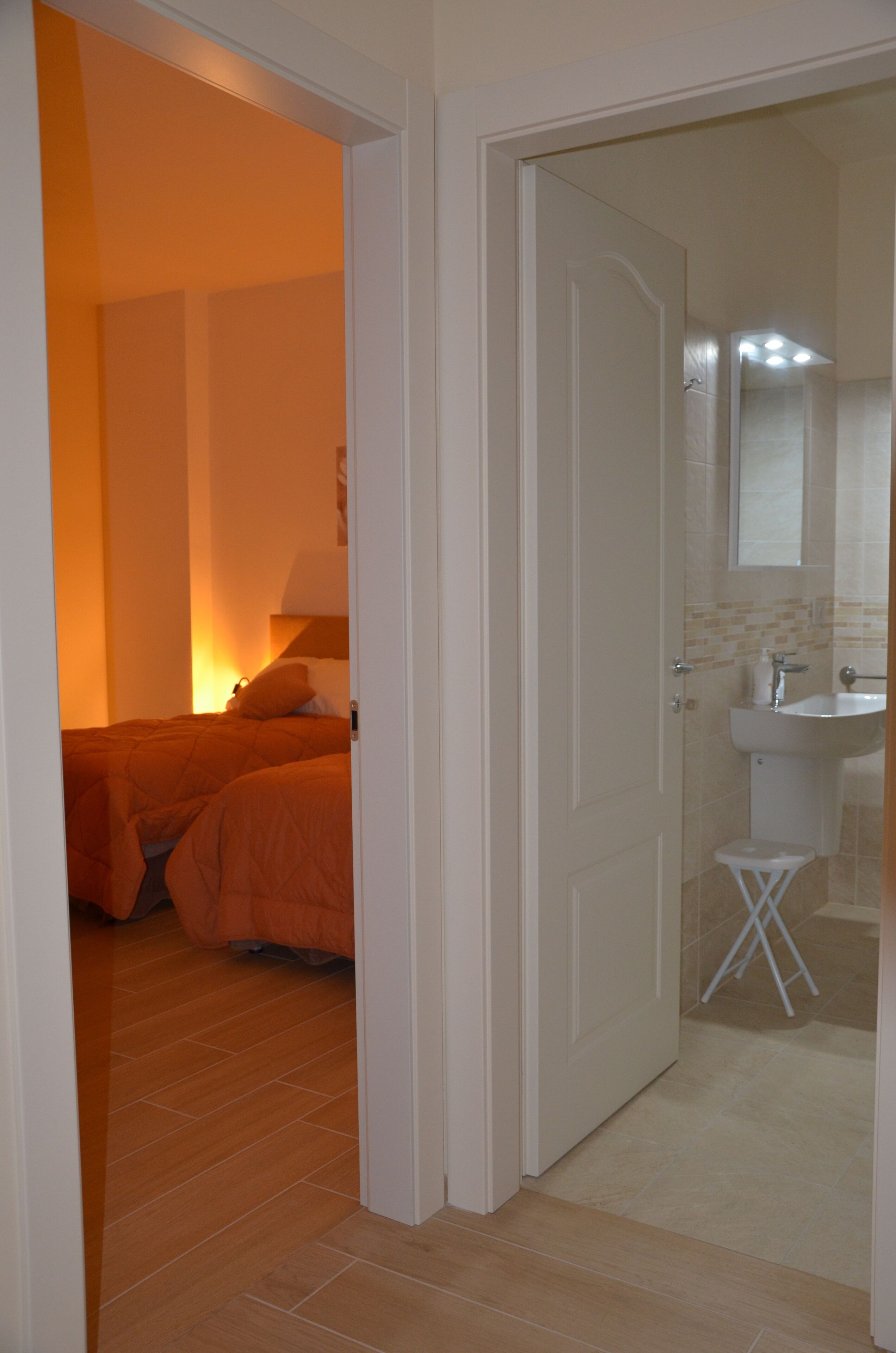 Une chambre à coucher avec un lit, une table de chevet et une commode. Il y a une salle de bain avec un lavabo et un miroir.