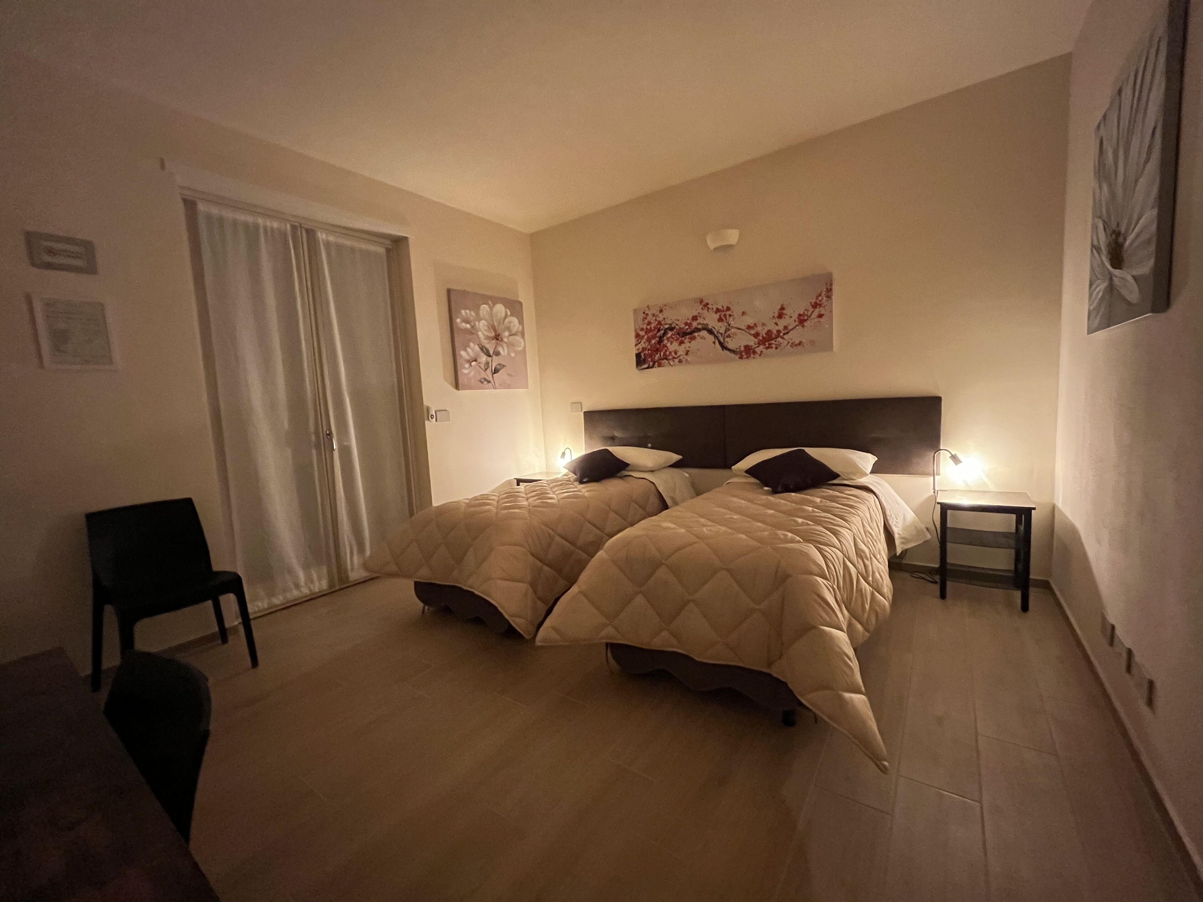 Quarto de hotel com duas camas, uma cadeira, uma escrivaninha e um quadro na parede.