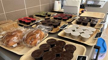 Mostrador de panadería con diversos productos horneados y vasitos de chocolate.