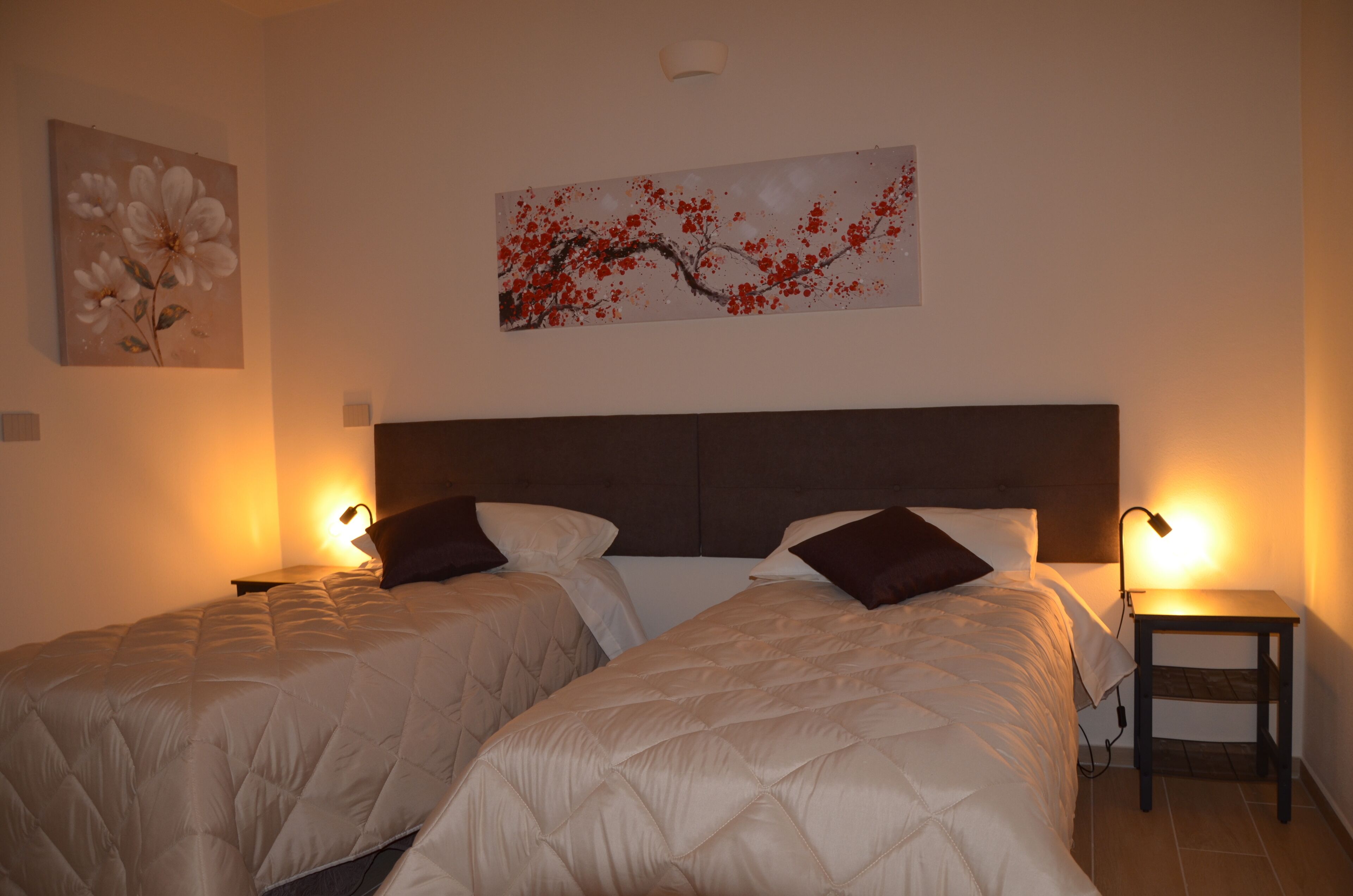 Quarto de hotel com duas camas, uma mesa de cabeceira e obras de arte nas paredes.