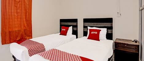 A hotel room with two beds, each with a red and white patterned bedspread, a wooden nightstand, and a red curtain.