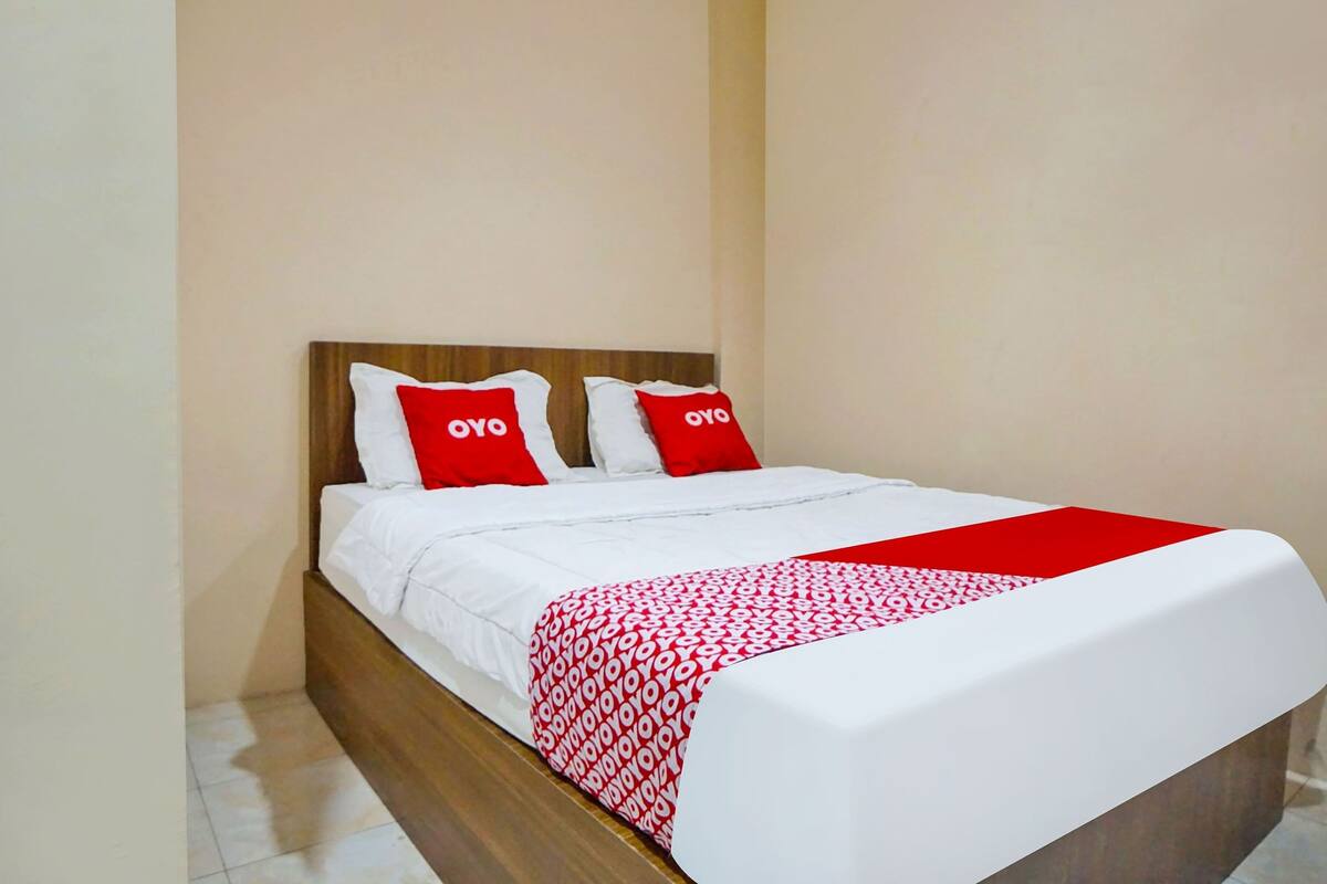 A neatly made bed with white bedding and red accents, including pillows and a blanket.