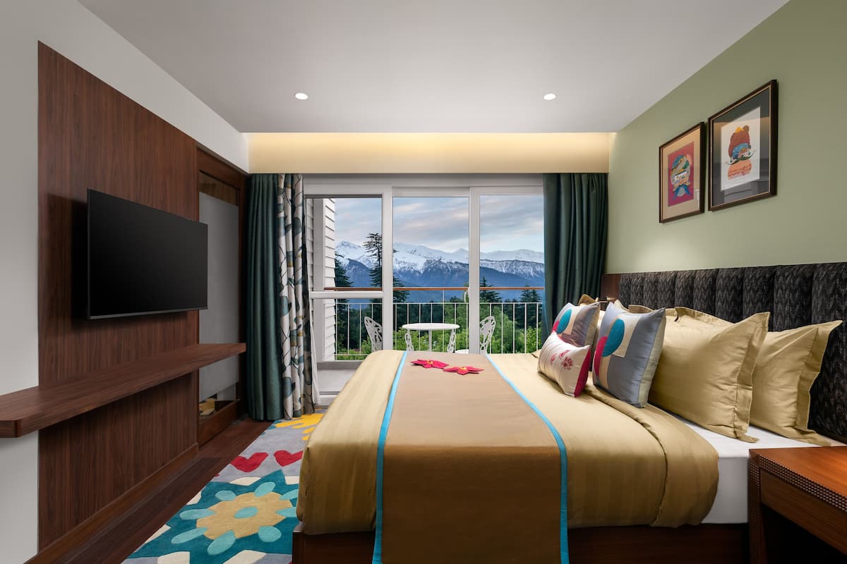 A hotel room with a bed, a TV, a balcony with a mountain view, and a window with curtains.