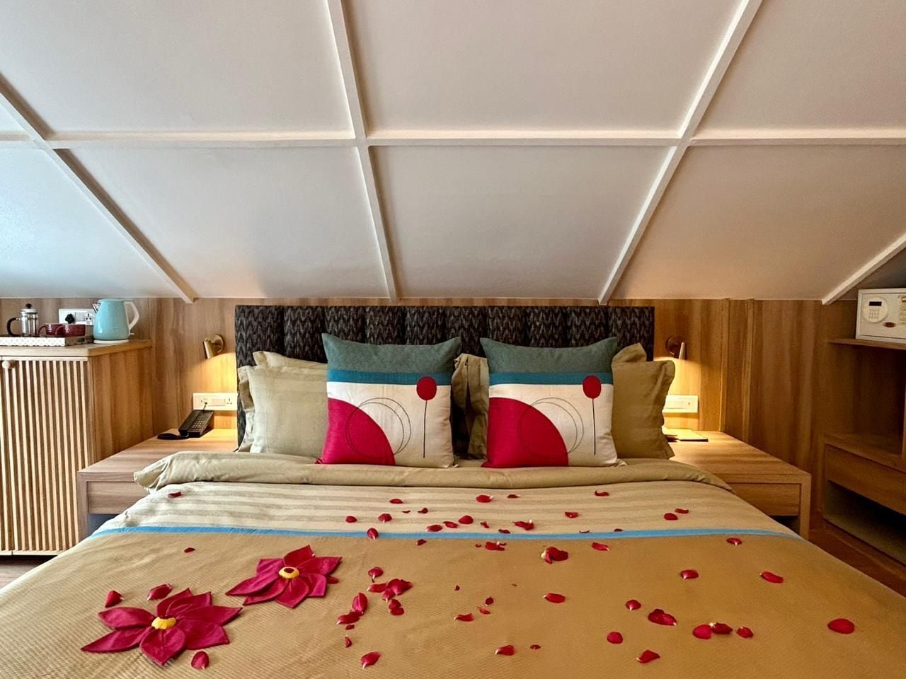 A hotel room with a bed, two bedside tables, a nightstand, a wall-mounted TV, and a wooden headboard.