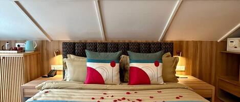 A hotel room with a bed, two bedside tables, a nightstand, a wall-mounted TV, and a wooden headboard.