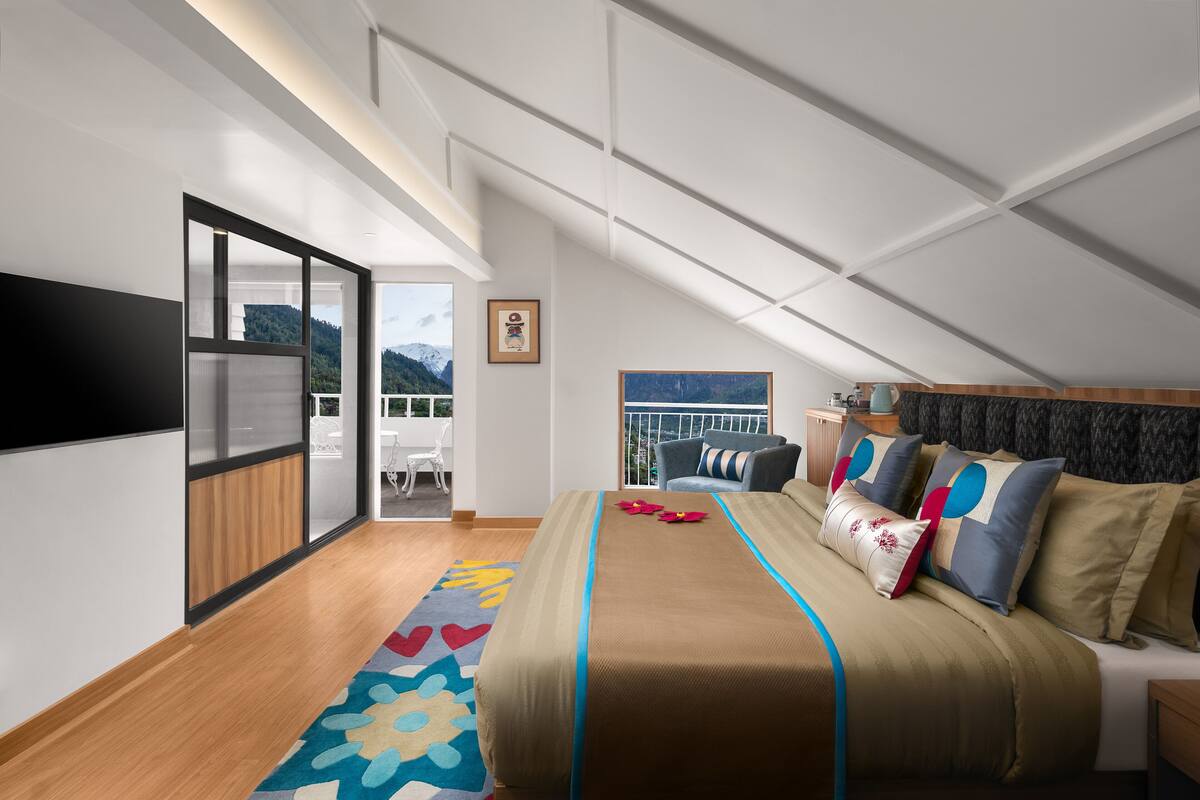 A modern bedroom with a large bed, a view of the mountains, and a balcony with a table and chairs.