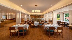 Un restaurant spacieux doté d’un plancher en bois, de nombreuses tables à manger recouvertes de nappes blanches et entourées de chaises, ainsi que d’un lustre central.