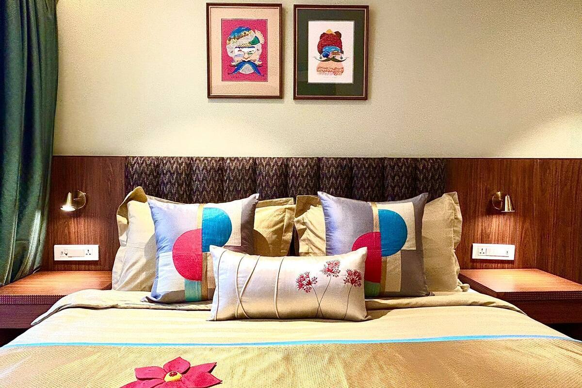 A hotel room with a bed, two bedside tables, a clock, and two framed pictures on the wall.