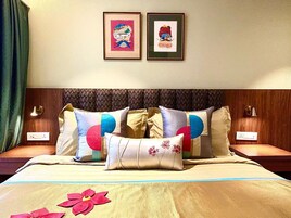 Habitación de hotel con una cama, dos mesitas de noche, un reloj y dos cuadros en la pared.
