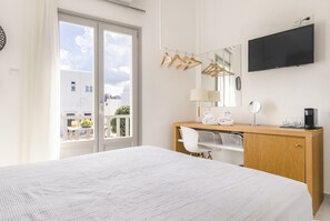 Habitación de hotel con cama, escritorio de madera, espejo, televisor y balcón con vista a edificios.