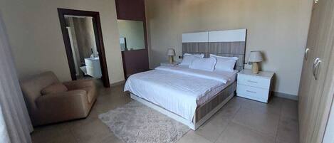 A bedroom with a bed, nightstands, a chair, and a large mirror.