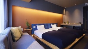 Een moderne hotelkamer met een groot bed, een bank, een klein tafeltje met een plant en een bureau met een waterkoker.