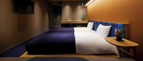 A hotel room with a large bed, a small desk, a TV mounted on the wall, and a small table with a plant.