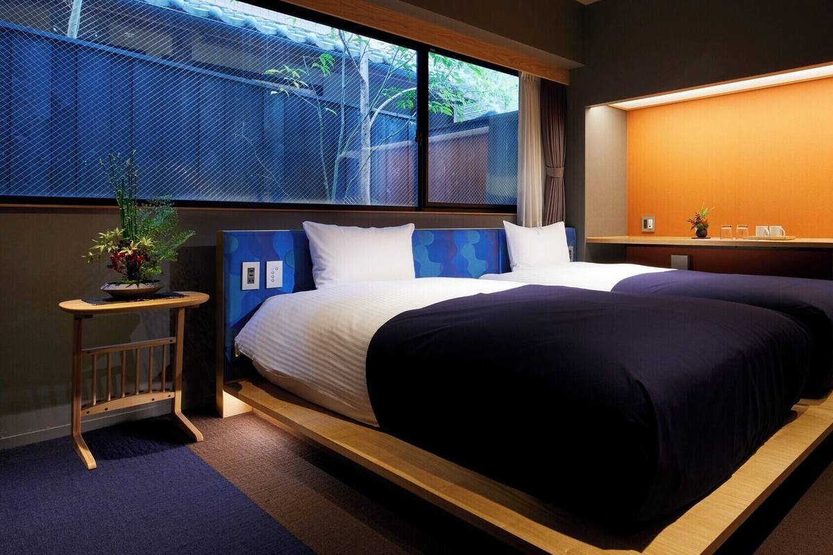 Een hotelkamer met een groot bed, een bureau en een raam met uitzicht op een schutting en bomen.