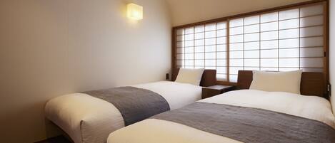 A hotel room with two beds, a nightstand, a wall-mounted light, and a shoji screen.