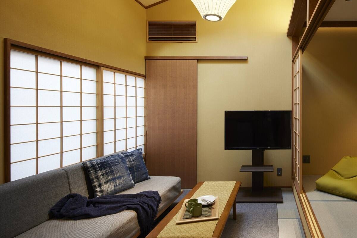 Een traditionele Japanse kamer met tatami vloerbedekking, een lage houten tafel met dienblad, een bank met kussens, een televisie en een schuifdeur.