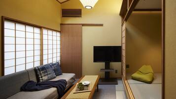 A traditional Japanese-style room with tatami flooring, a low wooden table with a tray, a sofa with cushions, a television, and a sliding door.