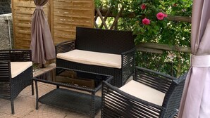 An outdoor seating area with wicker furniture under a canopy, surrounded by greenery and a tiled roof in the background. - The Sea Flower (Sanremo)