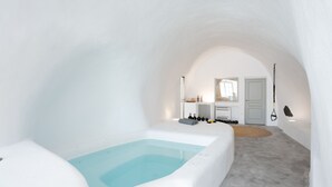 Una habitación moderna con decoración en blanco, una bañera grande, una kitchenette pequeña y una puerta que da a otra habitación.