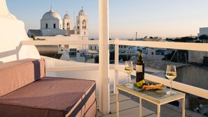 Una terraza con una pérgola blanca, una mesa con una botella y copas, y vistas a edificios blancos con cúpulas.