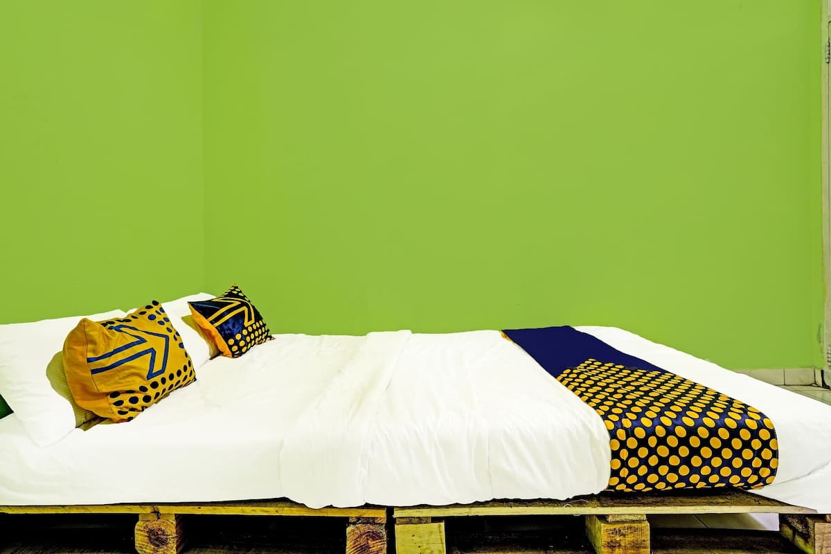 Ein Bett mit weißer Bettwäsche und zwei Kissen mit Muster, vor einer grünen Wand.