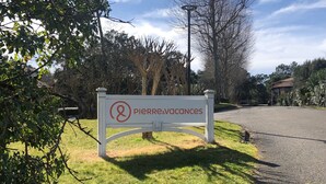 A sign for 'Pierre & Vacances' in a grassy area with trees and a paved path. - Sunny terrace overlooking golf course and forest.★ (Moliets et Maâ)