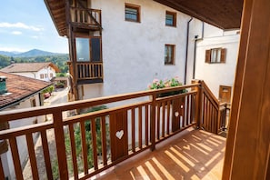 Un balcón con barandilla de madera y detalles con forma de corazón, con vistas a una calle con edificios y una montaña al fondo.