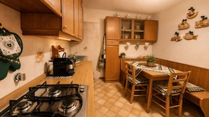 Una cocina con gabinetes de madera, estufa a gas, cafetera y una mesa de comedor con sillas.