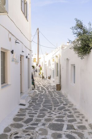 Uma rua estreita de calçada, ladeada por edifícios brancos com portas em arco e pequenas janelas.